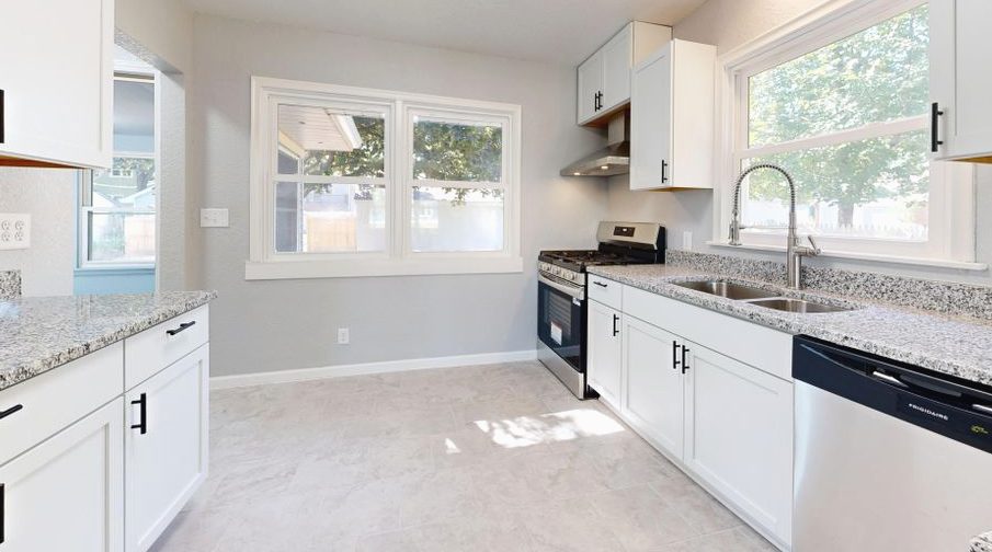Sunlit modern kitchen featuring granite countertops and sleek white cabinetry